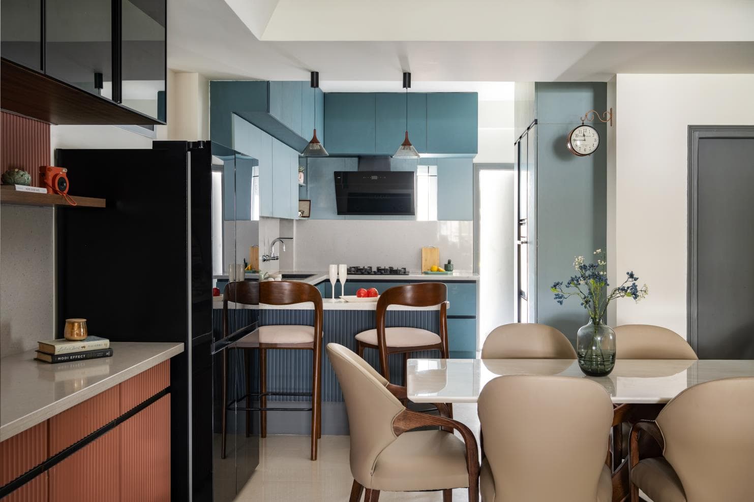 Kitchen with blue-grey cabinetry, pendant lights and walnut bar stools opening onto the dining area